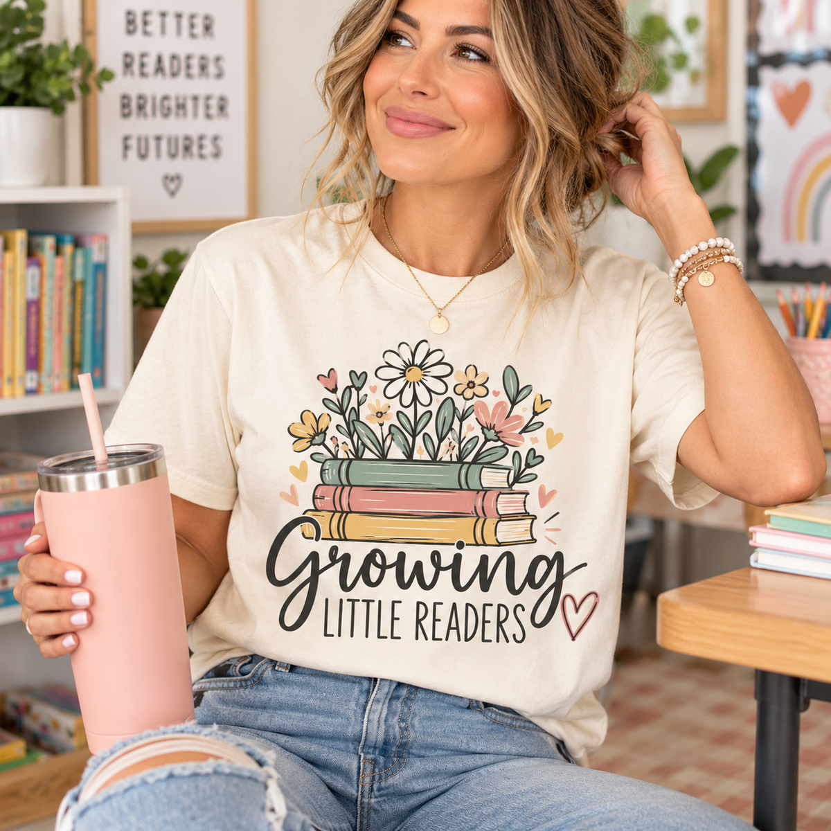 Teacher wearing an ivory Growing Little Readers Comfort Colors shirt featuring colorful books and flowers in a classroom setting.