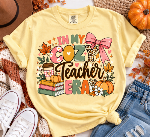 Butter Comfort Colors In My Cozy Teacher Era shirt with pumpkins, books, coffee, bow and colorful fall details styled in a cozy autumn flat lay.