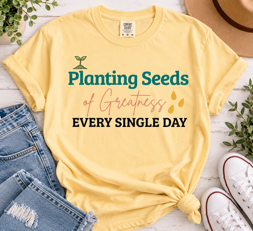 Butter Comfort Colors Planting Seeds of Greatness teacher shirt styled in a flat lay with jeans, white sneakers, greenery, and a hat.