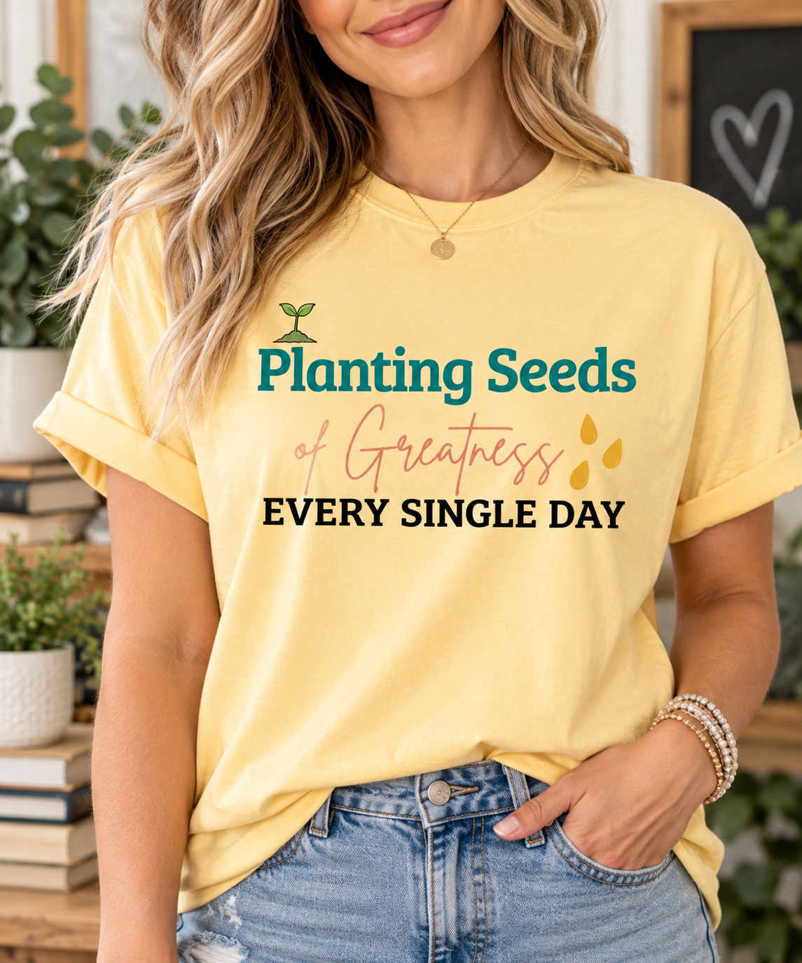 Teacher wearing a Butter Comfort Colors Planting Seeds of Greatness shirt with jeans in a warm classroom-inspired setting.