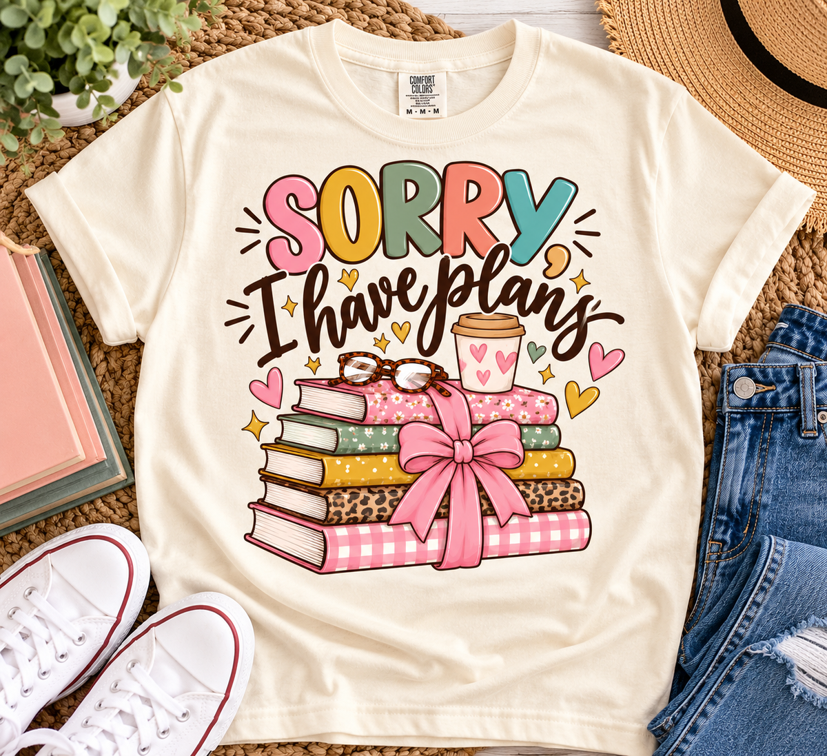 Ivory Comfort Colors Sorry I Have Plans book lover shirt with colorful books, pink bow, coffee and hearts styled in a cozy flat lay.