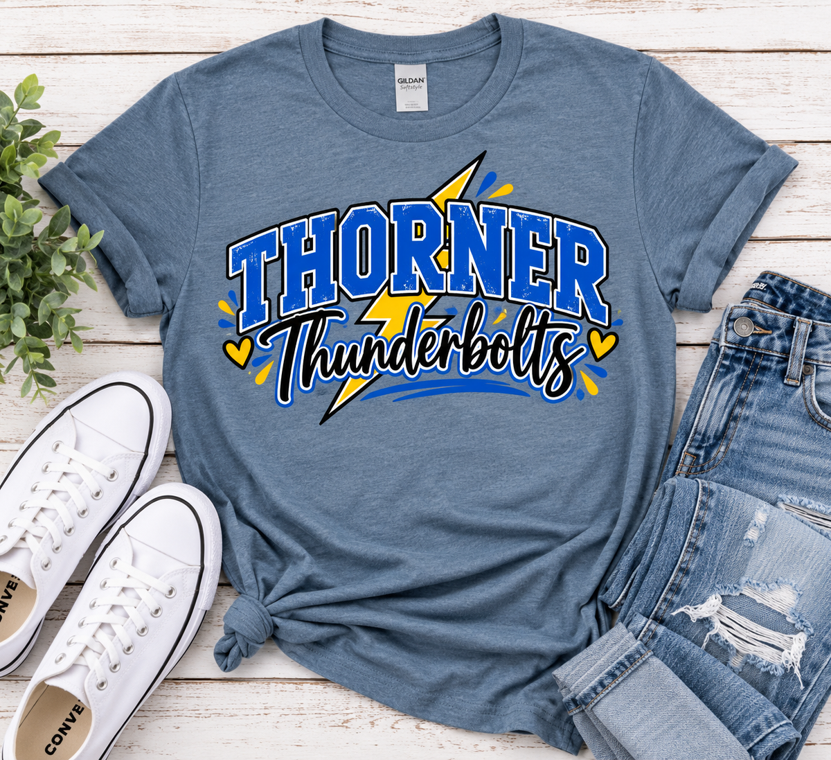 Blue Gildan Softstyle Thorner Thunderbolts spirit shirt with blue and gold varsity design styled with jeans and white sneakers.