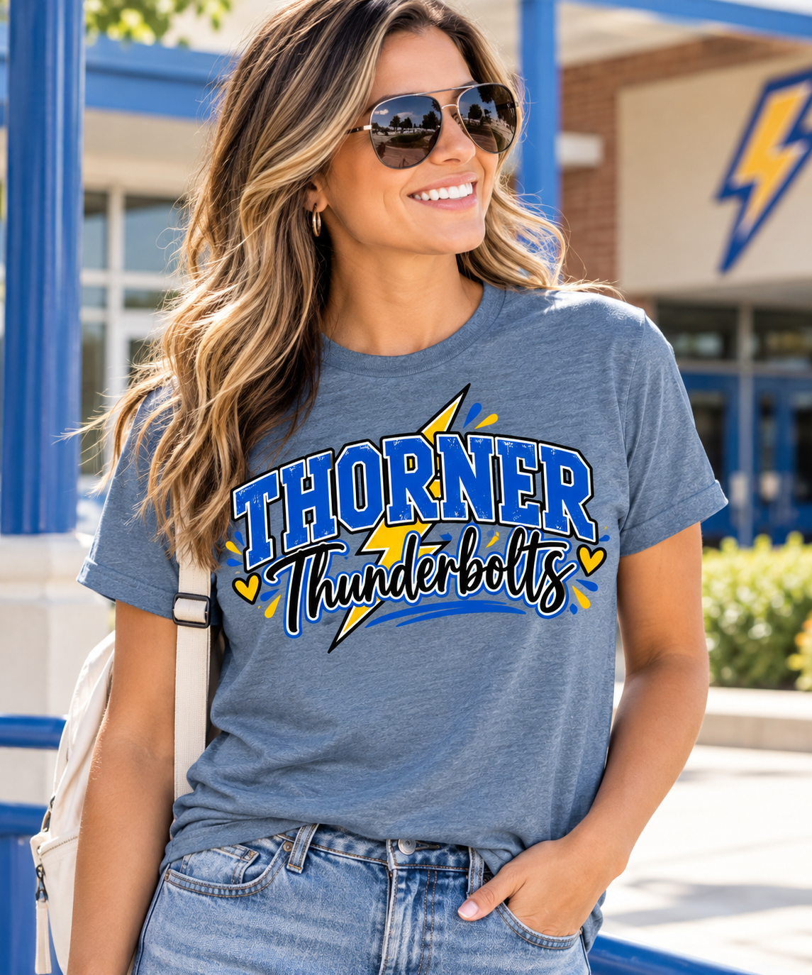 Woman wearing a blue Thorner Thunderbolts spirit shirt with a blue and gold varsity design outside a school.