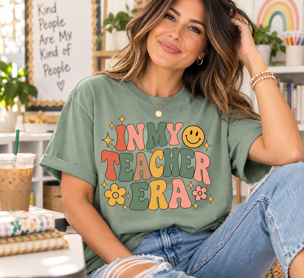 Teacher wearing a sage green Comfort Colors In My Teacher Era shirt with colorful retro lettering in a classroom setting.